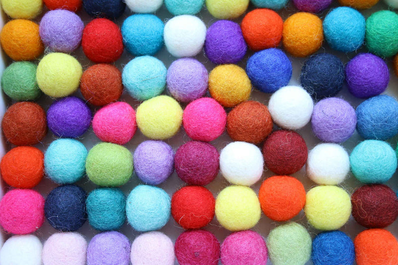 A close-up grid of small felt pom-poms in many bright colors, including orange, red, pink, purple, blue, teal, yellow, green, and white.